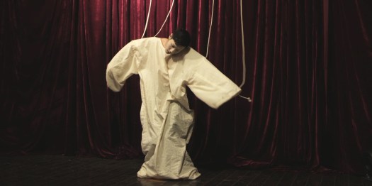 a human puppet on stage with strings tied to his hands